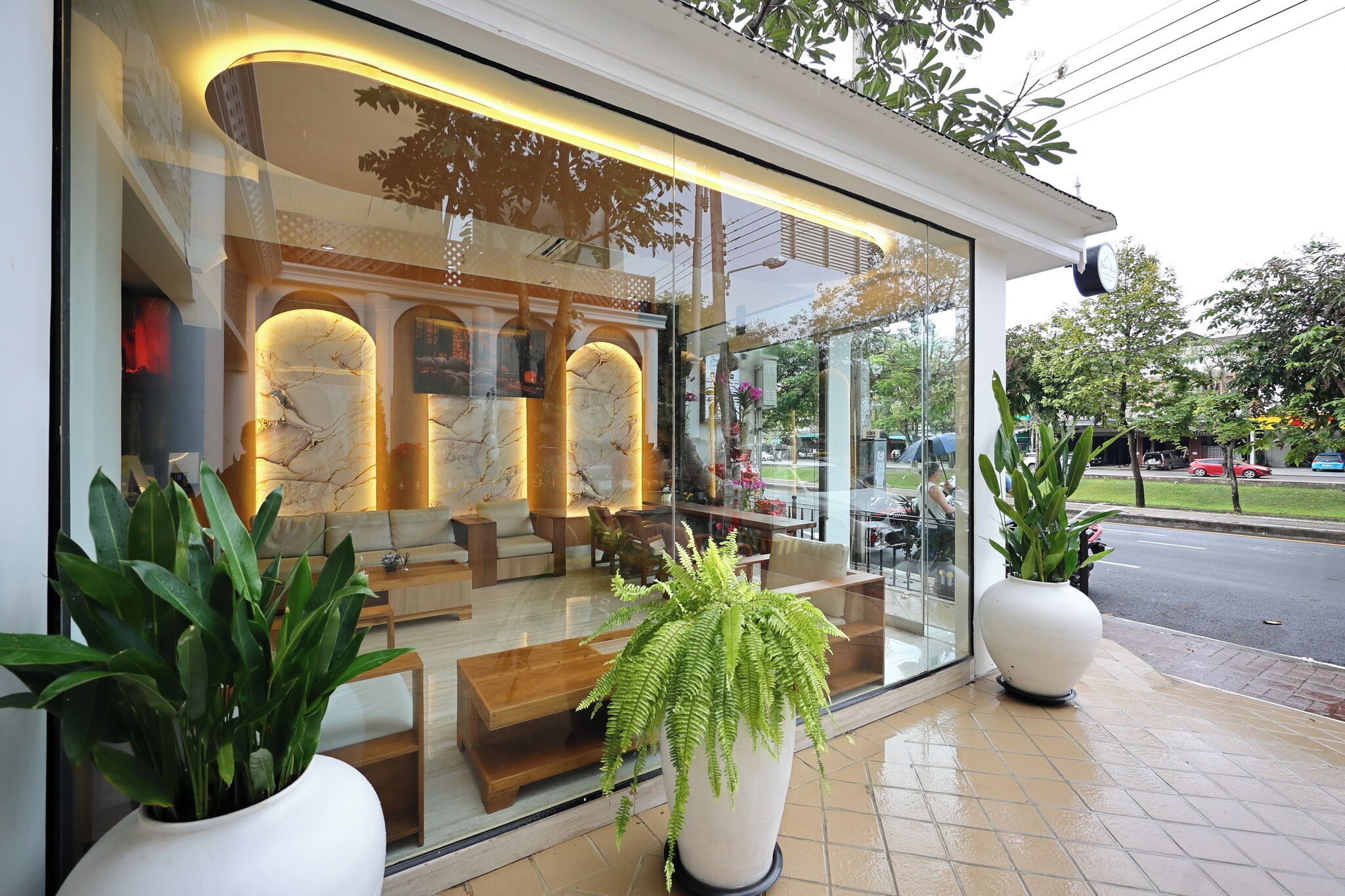 A modern hotel lobby with a glass facade, seating area, and potted plants.