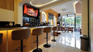 Eine moderne Bar mit hohen Hockern, einem Fernsehbild, das einen Kamin zeigt, und Blick ins Freie durch große Fenster.