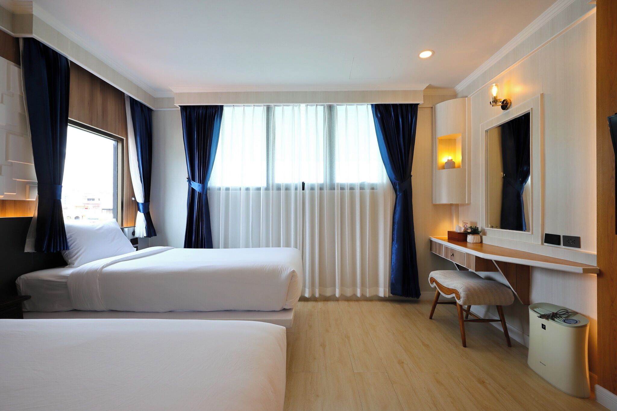 Habitación de hotel con dos camas, un escritorio, una silla, un espejo y una ventana con cortinas.