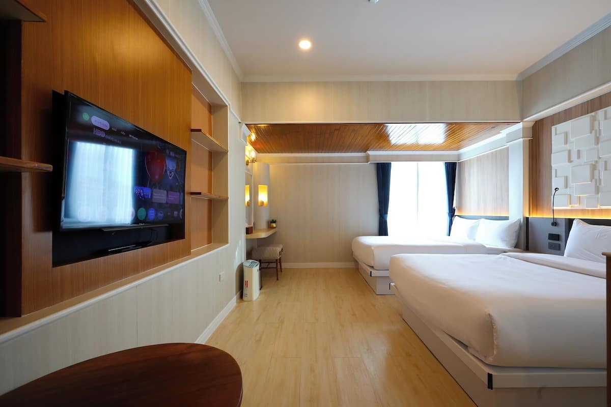 Een hotelkamer met een flatscreen televisie aan de muur, een bed, een nachtkastje en een zithoekje.