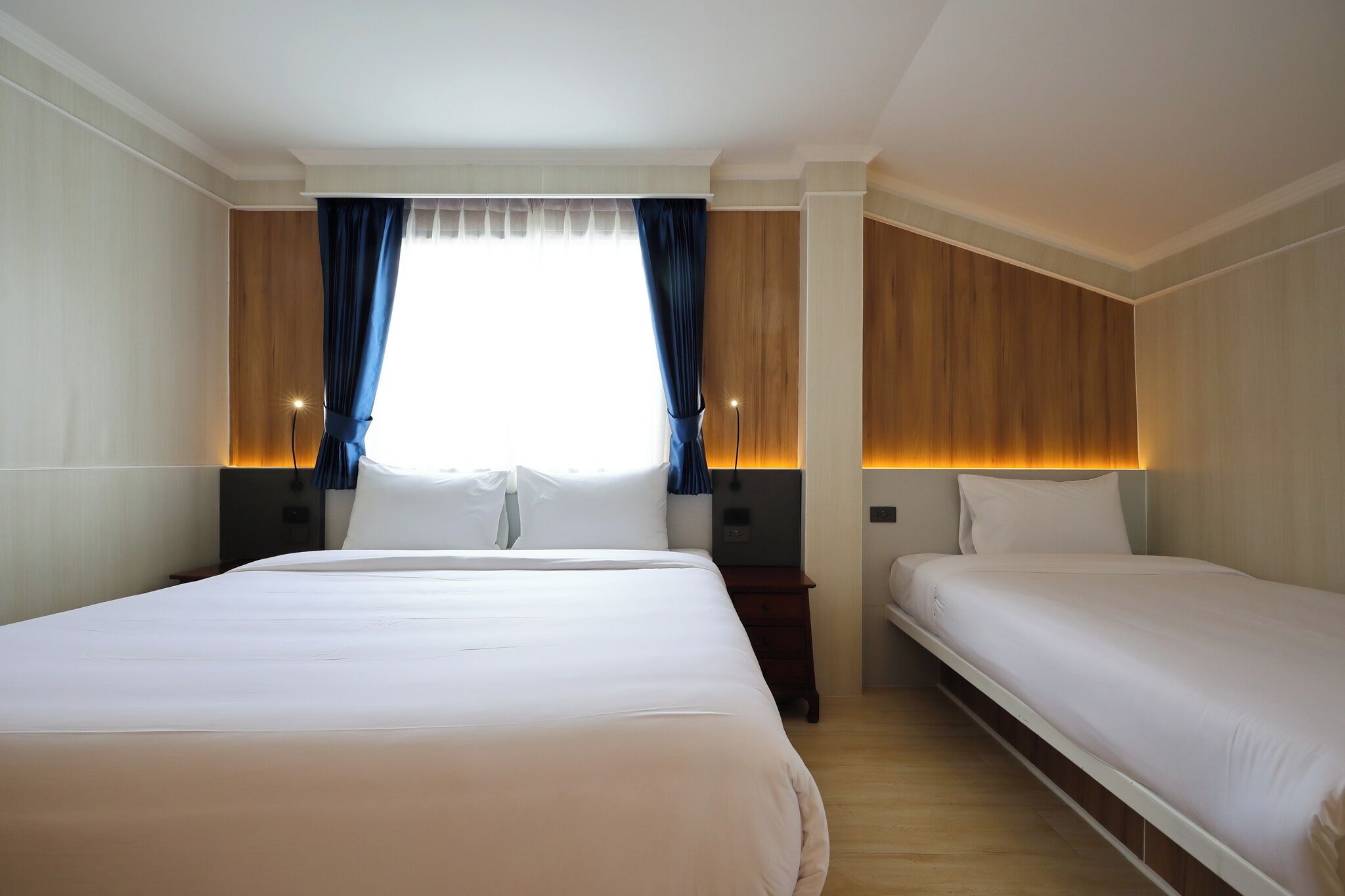 Habitación de hotel con dos camas, un ventanal grande con cortinas y un cabecero de madera.