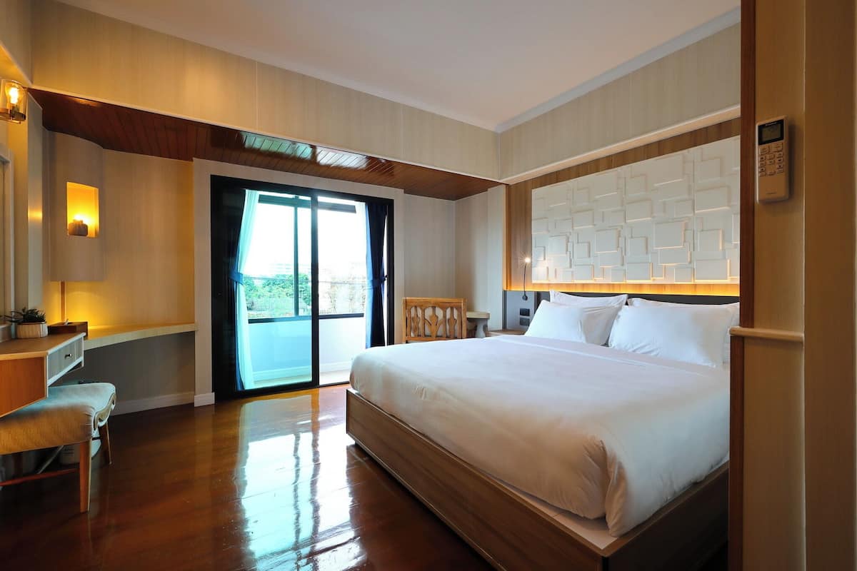 Een hotelkamer met een groot bed, een bureau en een stoel. Er is een schuifdeur naar een balkon.