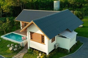 Une maison de plain-pied avec un toit en pente, une petite piscine et une allée pavée.