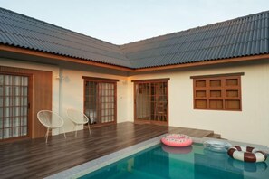 Un espace piscine doté d’une terrasse en bois, de deux chaises blanches et d’un flotteur.