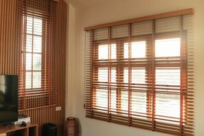 A room with a television on a stand, a window with wooden blinds, and a wall-mounted speaker. - Harper Pool Villa Khaoyai 3 Bedroom, 3 Bathroom (Pak Chong)