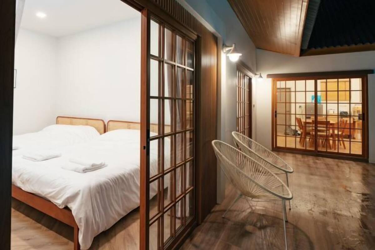 Una habitación con cama, una puerta corrediza de vidrio que da a un comedor y una silla.