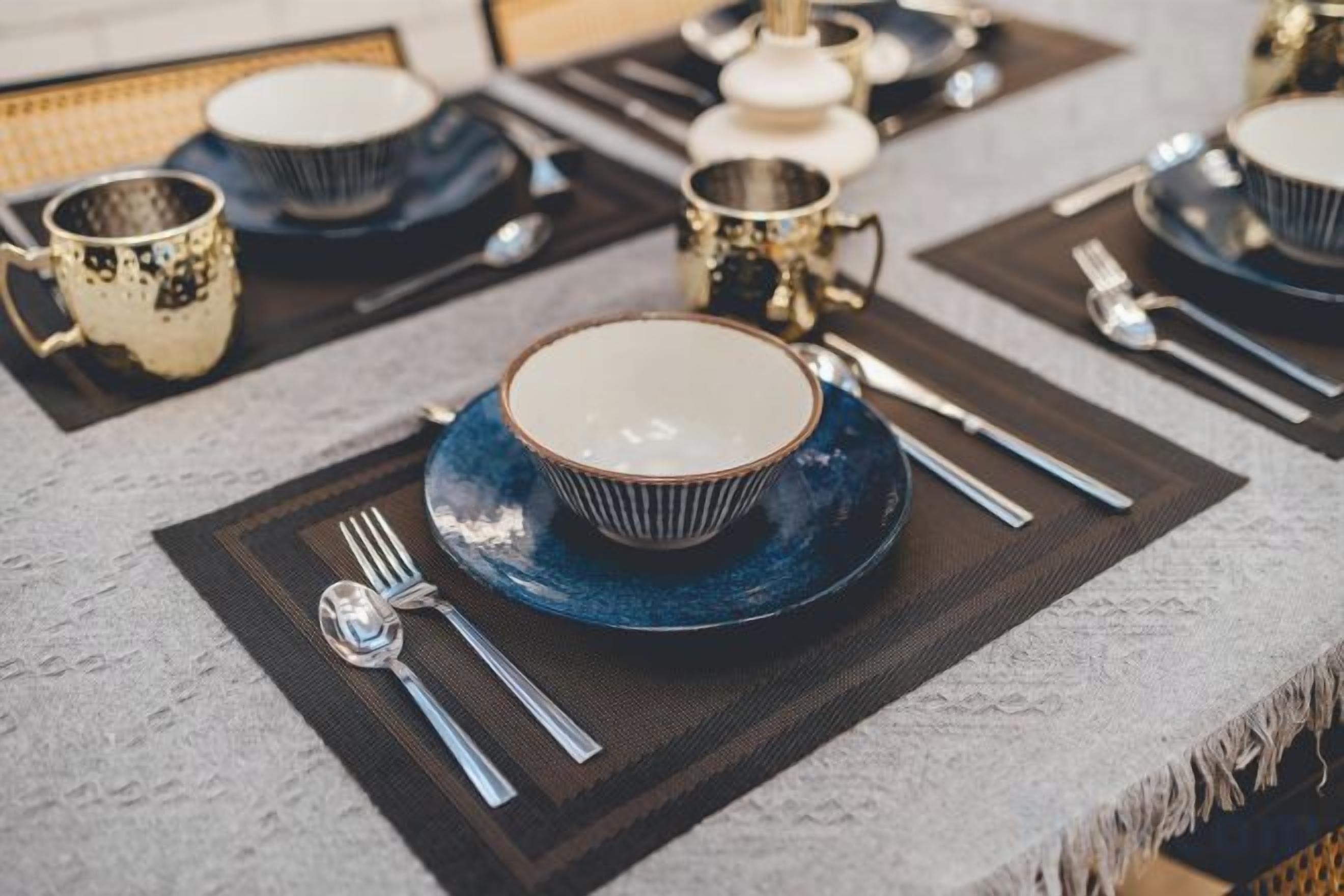A table set with a blue bowl, silverware, and a white plate on a textured tablecloth.