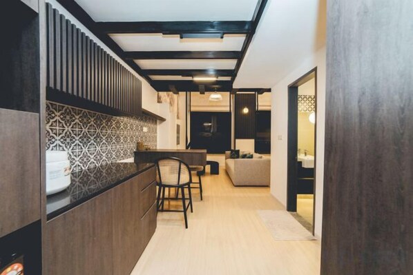 A modern kitchen with a dark wood countertop, a patterned backsplash, and a dining area with a sofa and chairs. - Sunway GRID Residence Legoland (Iskandar Puteri)