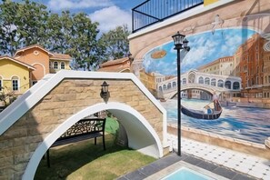 Une fresque représentant un pont et des bâtiments, une arche en pierre, un banc et un lampadaire.