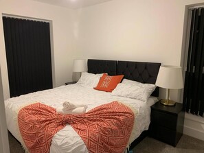 Un letto rifatto con un piumone bianco, due cuscini e una coperta rossa. Due lampade da comodino su poggiatesta neri.