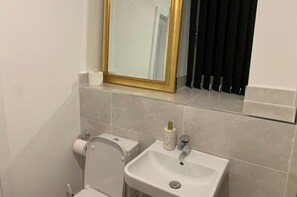 A bathroom with a toilet, sink, and mirror. - 4bed House - Direct Links Into Central London (South Ockendon)