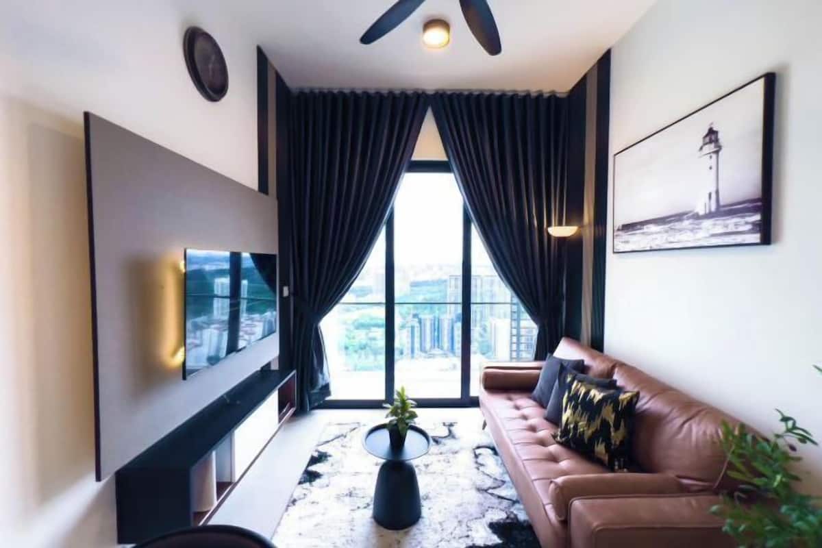 A modern living room with a sofa, a TV, a coffee table, and a view of the city through large windows.