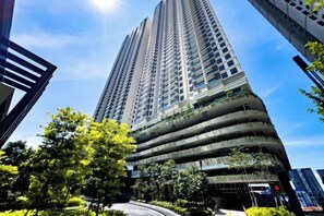 Ein Hochhaus mit mehreren Stockwerken, umgeben von Grünflächen und weiteren Gebäuden.