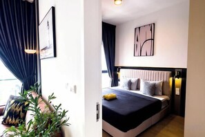 Ein Hotelzimmer mit Bett, Nachttisch, Kopfteil, Wandgemälde und einer Zimmerpflanze.