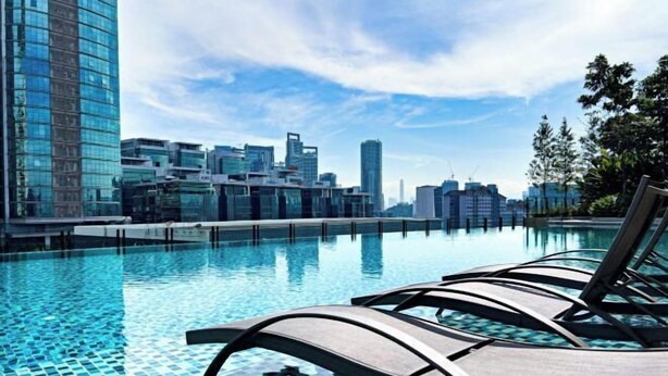 Une piscine moderne d’hôtel, dotée de chaises longues, offrant une vue sur les toits de la ville et dont le fond est recouvert de carrelage.