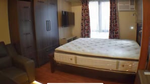 A bedroom with a large bed, a wardrobe, a television, and a window with curtains.