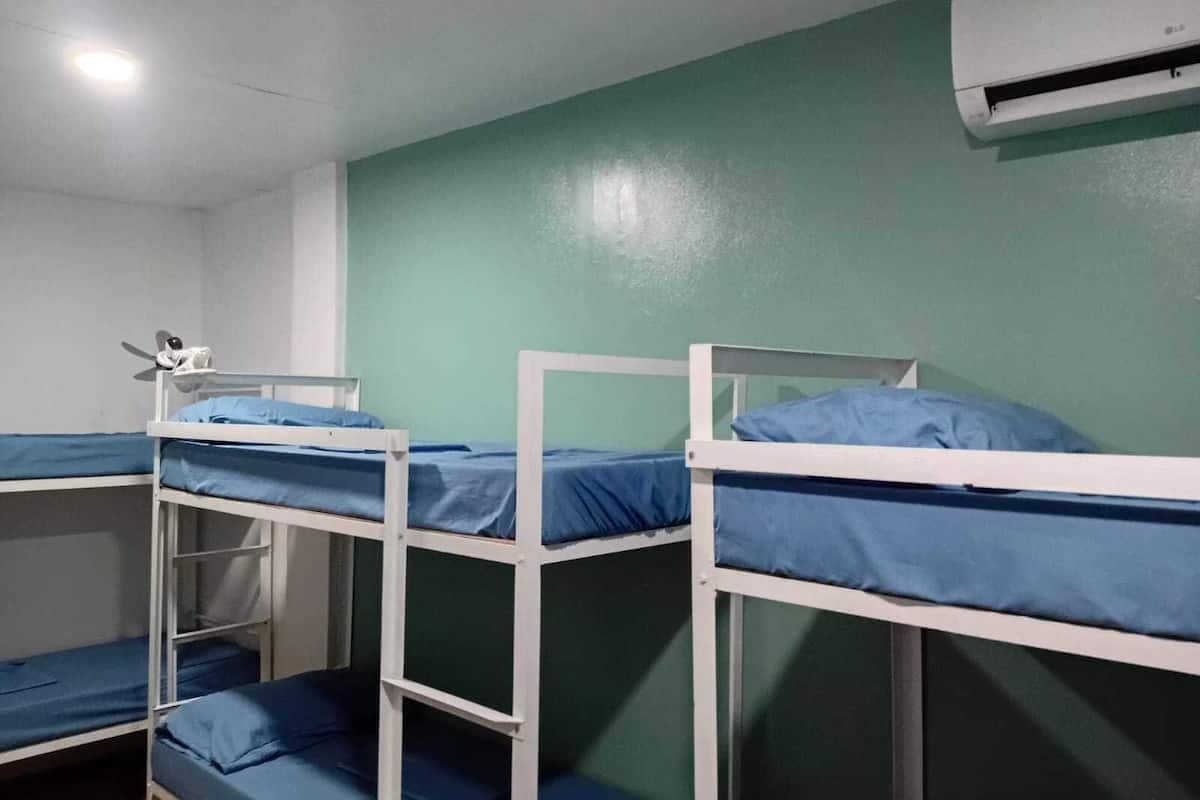 Une chambre de dortoir avec des lits superposés, un ventilateur de plafond et un appareil de climatisation.