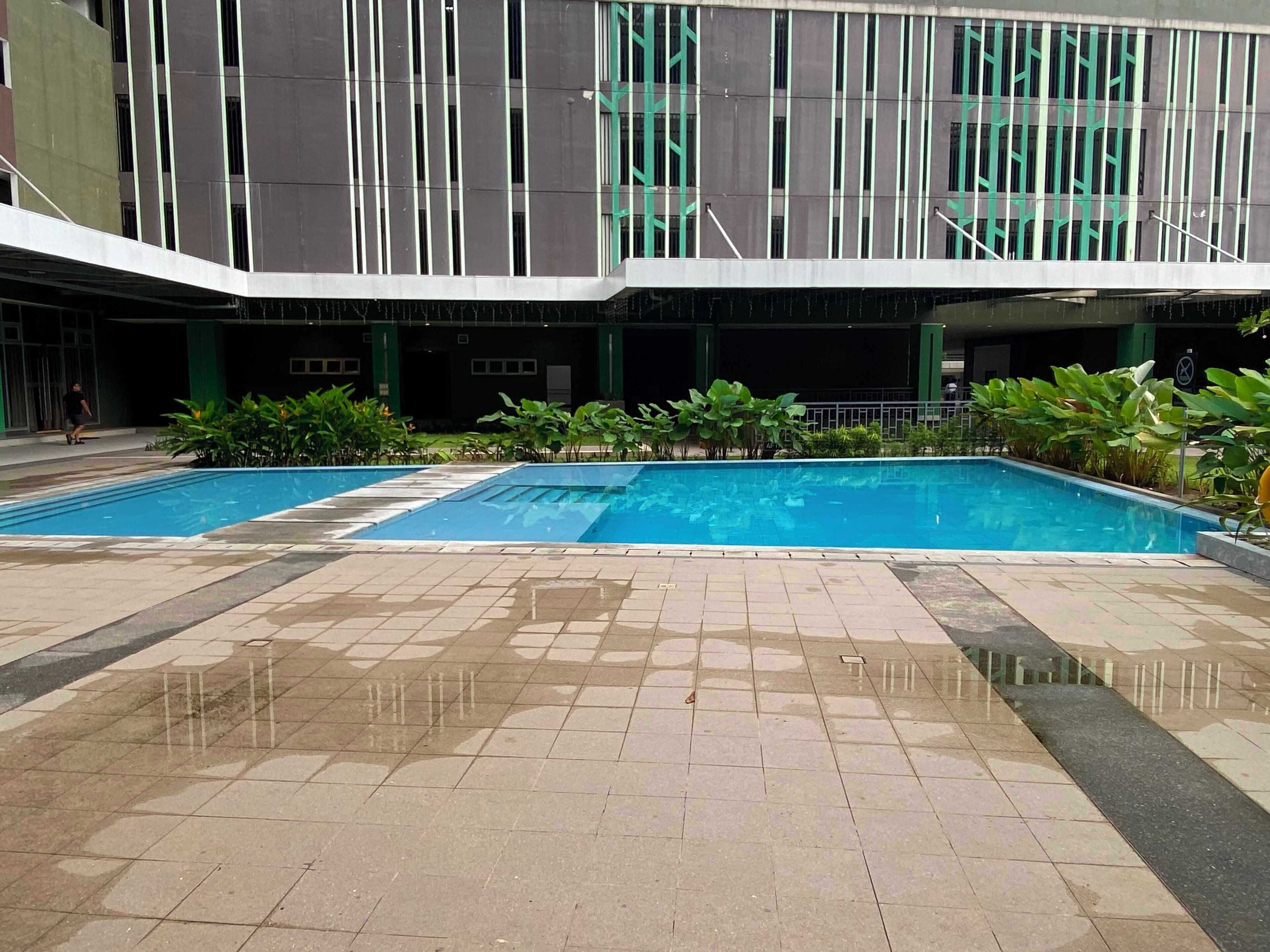 Ein Poolbereich mit zwei Pools, umgeben von einer gefliesten Terrasse und viel Grün.