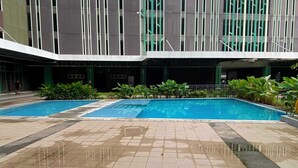 A swimming pool area with two pools, surrounded by a tiled patio and greenery.