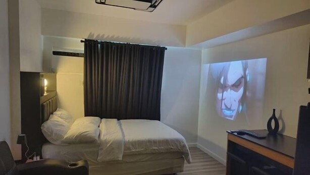 A hotel room with a bed, a desk, a projector, and a wall-mounted TV. - New Minimalist Condo at Cebu I.T. Park Avida Riala (Cebu City)