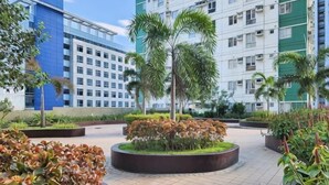 A courtyard with a circular garden, palm trees, and a modern building with a grid pattern in the background. - New Minimalist Condo at Cebu I.T. Park Avida Riala (Cebu City)