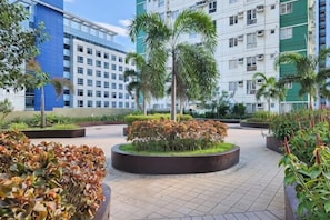 A courtyard with a circular garden, palm trees, and a modern building with a grid pattern in the background. - New Minimalist Condo at Cebu I.T. Park Avida Riala (Cebu City)