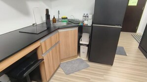 A compact kitchen with a black countertop, wooden cabinets, a built-in sink, a refrigerator, and a small trash bin. - New Minimalist Condo at Cebu I.T. Park Avida Riala (Cebu City)