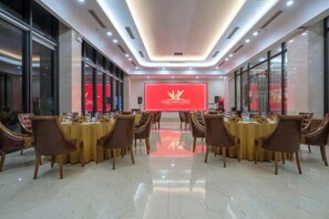 A conference room with round tables and chairs, a large screen at the front, and a modern ceiling design. - Hung Vuong Hotel (Mong Cai)
