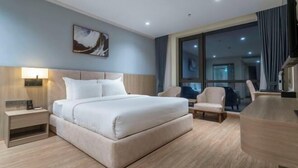 A modern hotel room with a large bed, a bedside table, a chair, and a large window offering a view of the city. - Hung Vuong Hotel (Mong Cai)