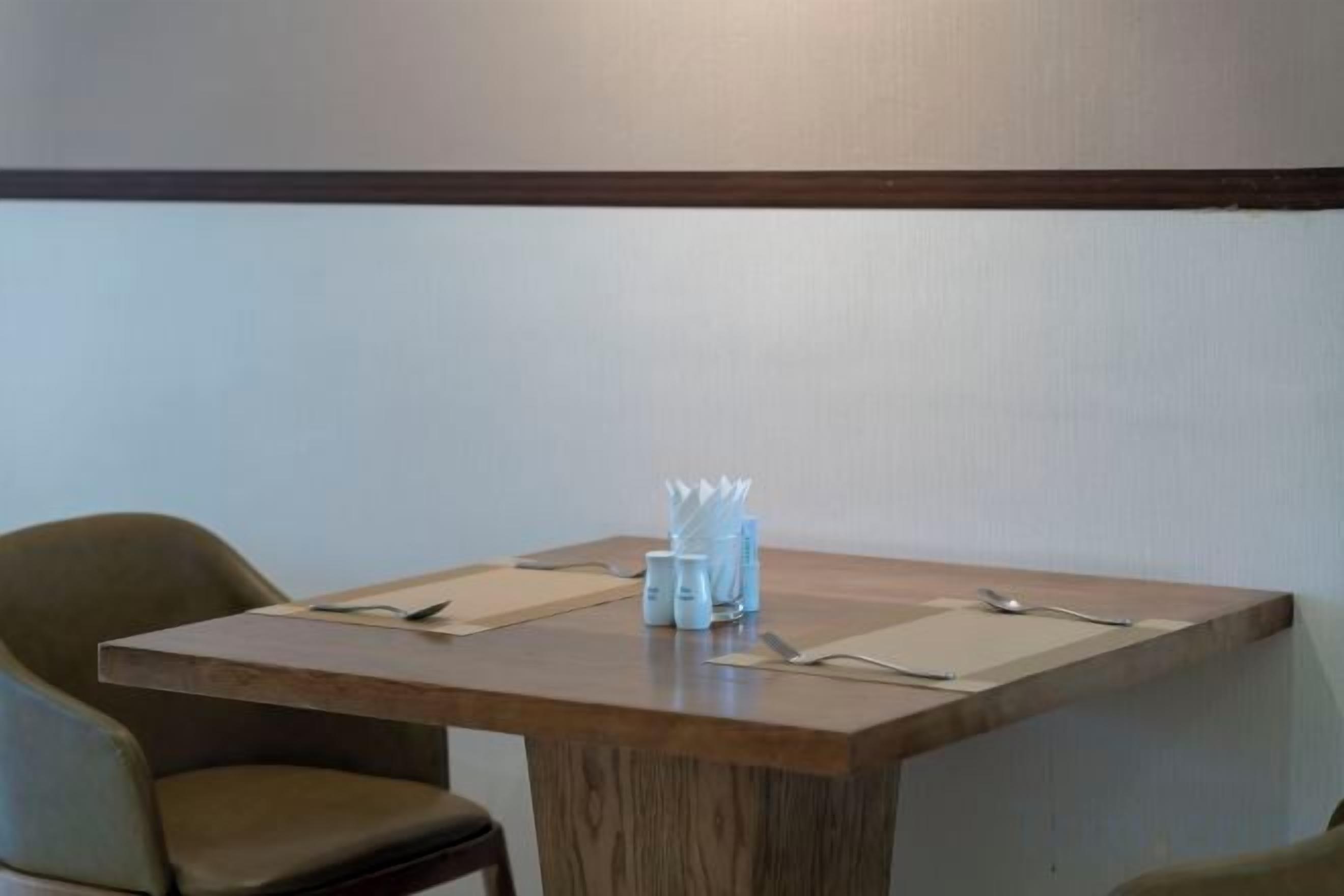 A table with a wooden top, two chairs, and a set of napkins and utensils.