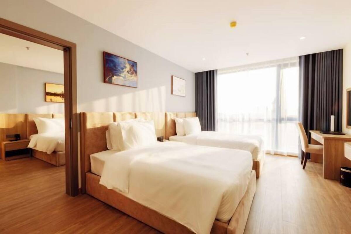 Ein Hotelzimmer mit zwei Betten, einem Schreibtisch und einem großen Fenster mit Vorhängen.