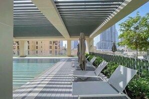 A rooftop pool area with lounge chairs and umbrellas, overlooking a cityscape. - bnbme Chic Apt w/ Balcony, 5 min to Burj Khalifa (Dubai)