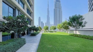 A modern building with a pathway leading to a grassy area, surrounded by trees and a view of a tall skyscraper in the background. - bnbme Chic Apt w/ Balcony, 5 min to Burj Khalifa (Dubai)