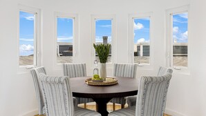 Un comedor con una mesa redonda, cuatro sillas estampadas, un florero con follaje y una bandeja con frutas y queso.