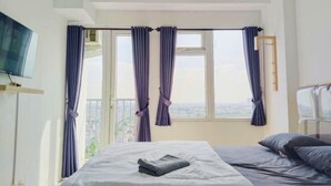 A hotel room with a bed, a TV on the wall, and a window with curtains.