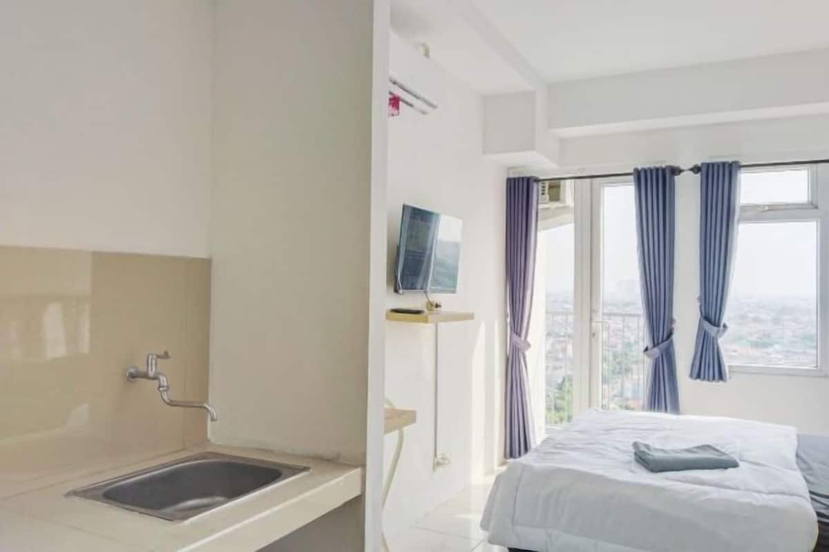 Quarto de hotel com cama, janela com cortinas, televisão fixada na parede e pia.