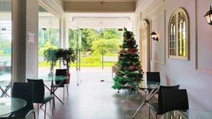 A spacious indoor area with a glass table and chairs, a Christmas tree, and a view of greenery outside.