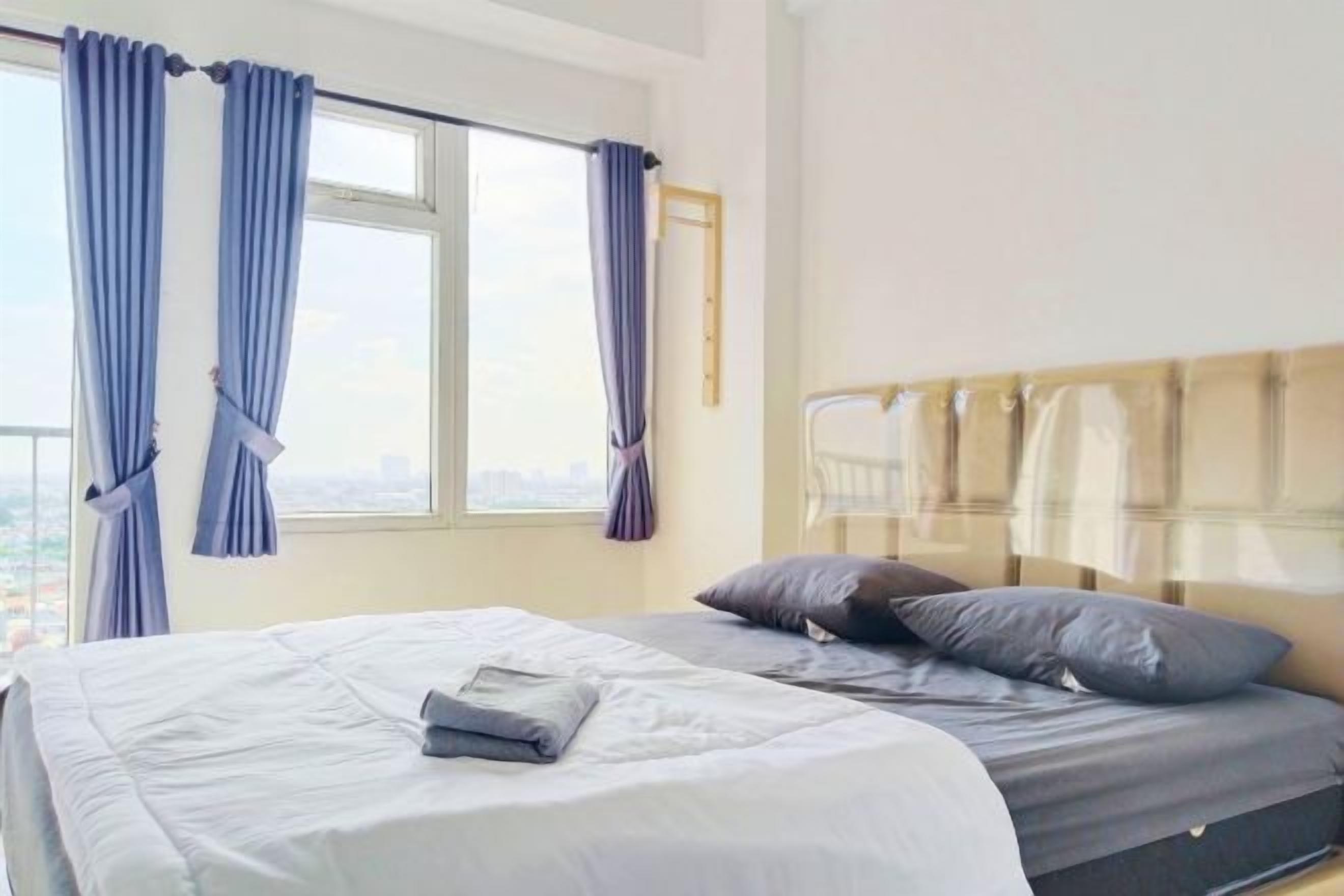 A hotel room with a bed, a window with curtains, and a view of the city.