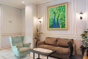 Una habitación con un sofá marrón, un sillón azul claro, una mesita de centro y un cuadro de pavos reales en la pared.