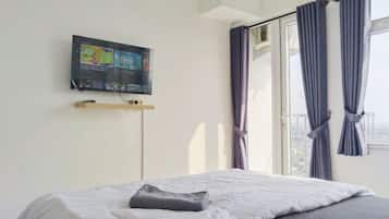 Ein Schlafzimmer mit einem Bett, einem an der Wand befestigten Fernseher und einem Fenster mit Vorhängen.