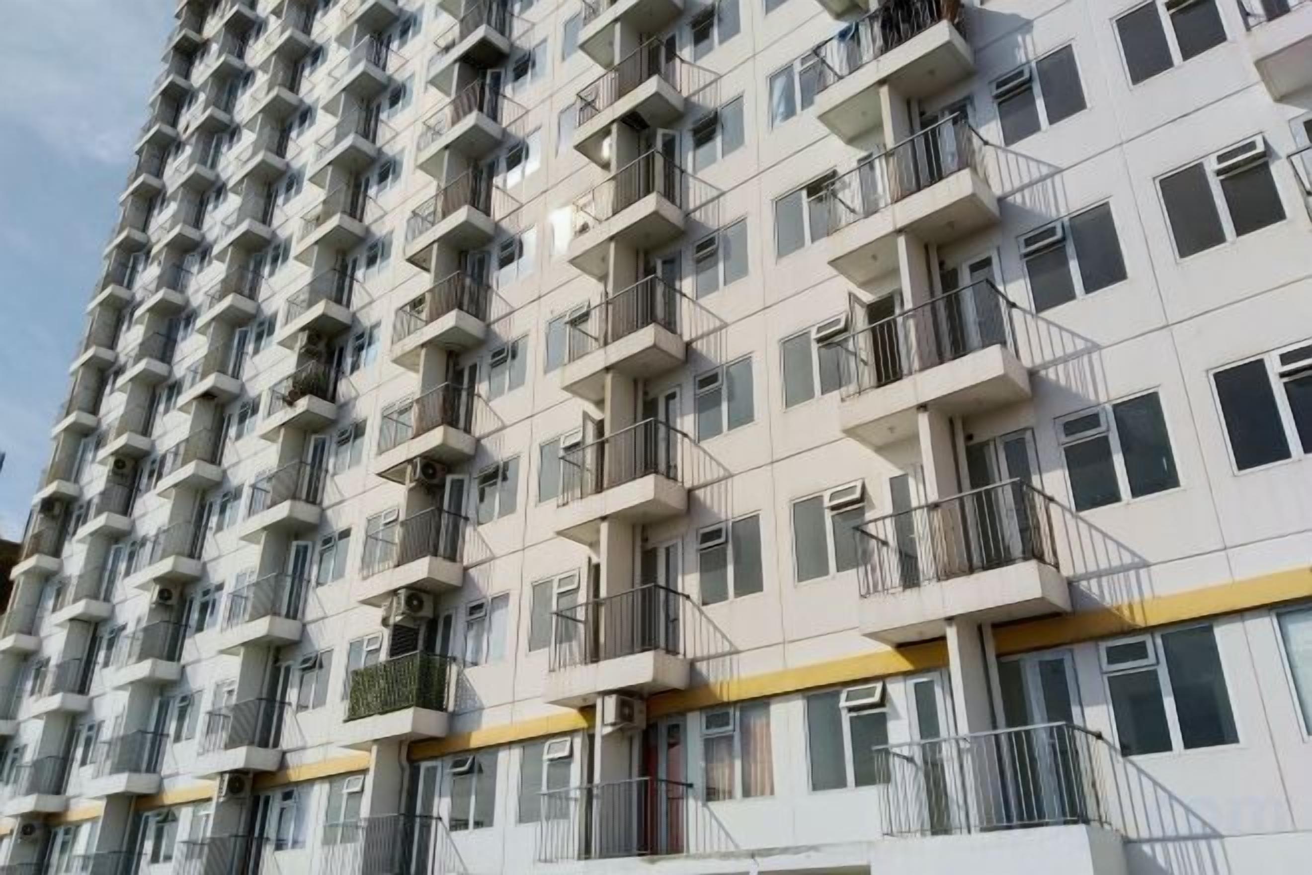 A multi-story residential building with balconies, windows, and a yellow stripe on the lower facade.