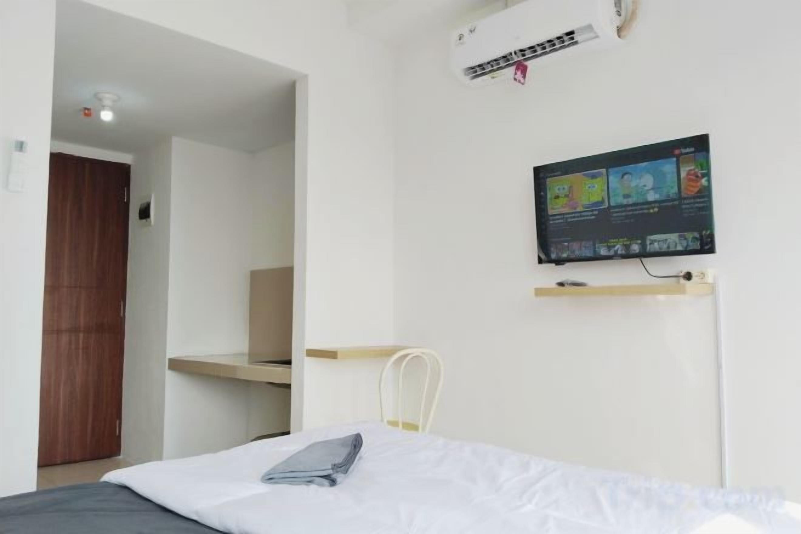 A bedroom with a bed, a TV mounted on the wall, a desk, and a chair.