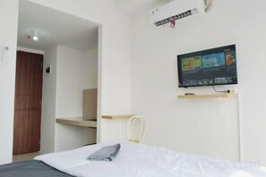 A bedroom with a bed, a TV mounted on the wall, a desk, and a chair. - Nusantara Metropolitan Park By Reccoma (North Bekasi)