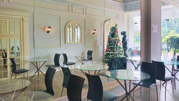 A hotel lobby with round glass tables and black chairs, a Christmas tree, and a large window with a view of greenery.