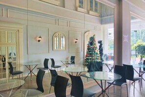 A hotel lobby with round glass tables and black chairs, a Christmas tree, and a large window with a view of greenery. - Nusantara Metropolitan Park By Reccoma (North Bekasi)