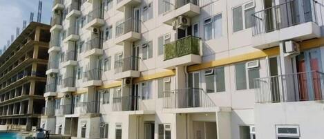 A multi-story hotel with balconies, a swimming pool, and a clear sky.