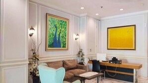A reception area with a reception desk, a light blue armchair, a brown sofa, and a painting of peacocks on the wall.
