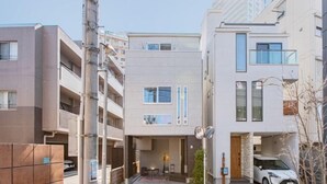 A modern apartment building with a central entrance, a covered parking area, and a white car parked in front. - Ikebukuro Japandi Villa (Tokyo)