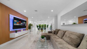 A modern living room with a large flat-screen TV mounted on a wooden wall, a brown sofa, and a glass coffee table.