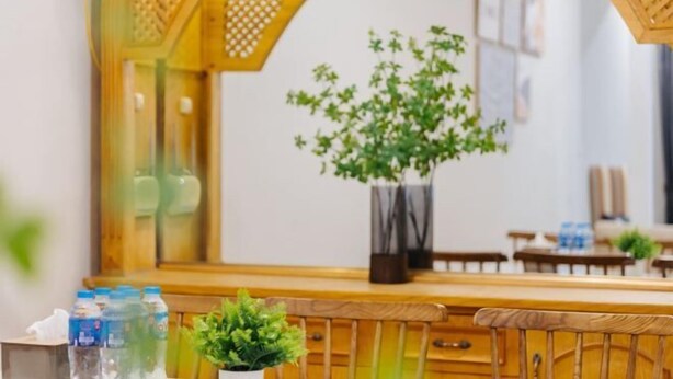 A room with a wooden bench, a small potted plant, and a mirror reflecting a plant and a wall with framed pictures. - VietHOME - 22 Pho Hue - Duplex 3 4 (Hanoi)